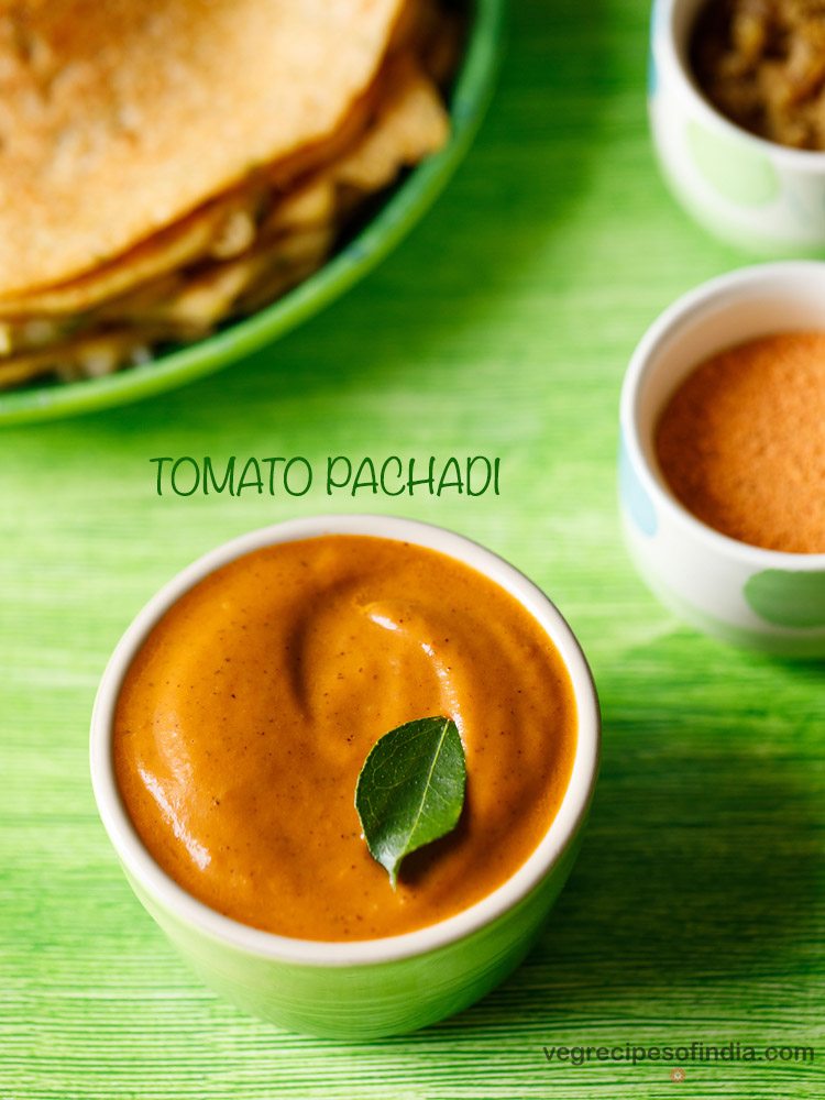 tomato pachadi garnished with a curry leaf, served in a light green colored small bowl with dosas kept on a light green colored platter and text layovers.