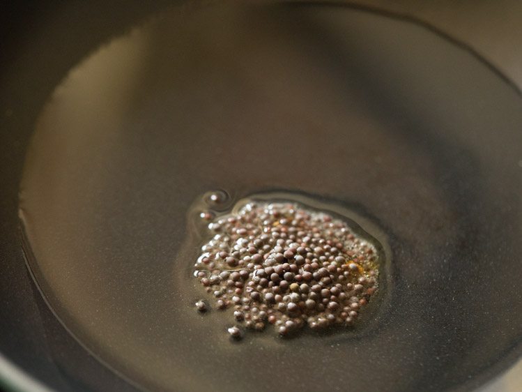 mustard seeds added to hot oil in pan for making thakkali pachadi. 