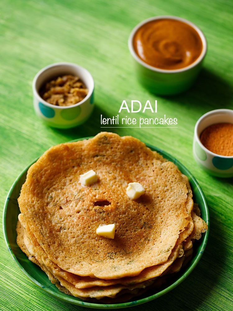 adai stacked and served on a green plate with butter cubes on top and bowls of chutney and sambar kept in the background and text layovers.
