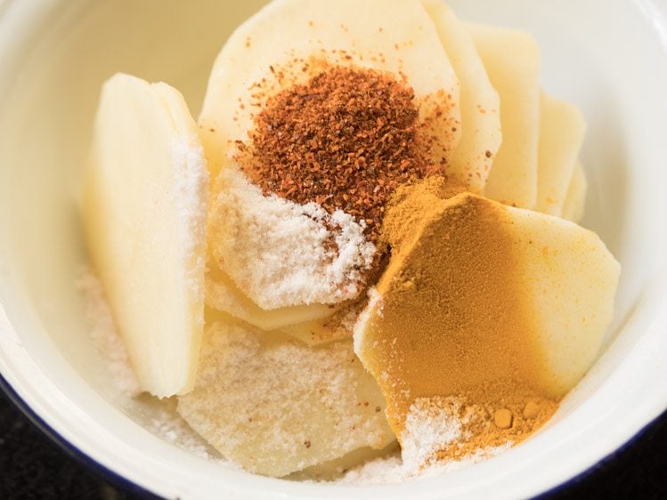 red chili powder, turmeric powder and salt added to the potato slices in a bowl. 