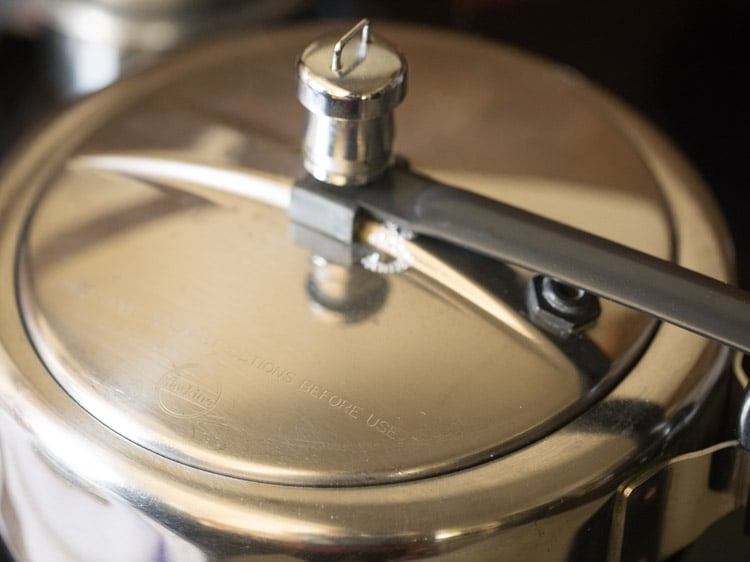 pressure cooker with the lid on for par cooking the bajra for making bajra khichdi recipe.