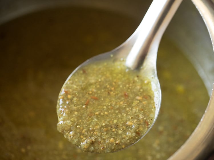 spoon showing  half-raw texture of bajra khichdi after first pressure cook.