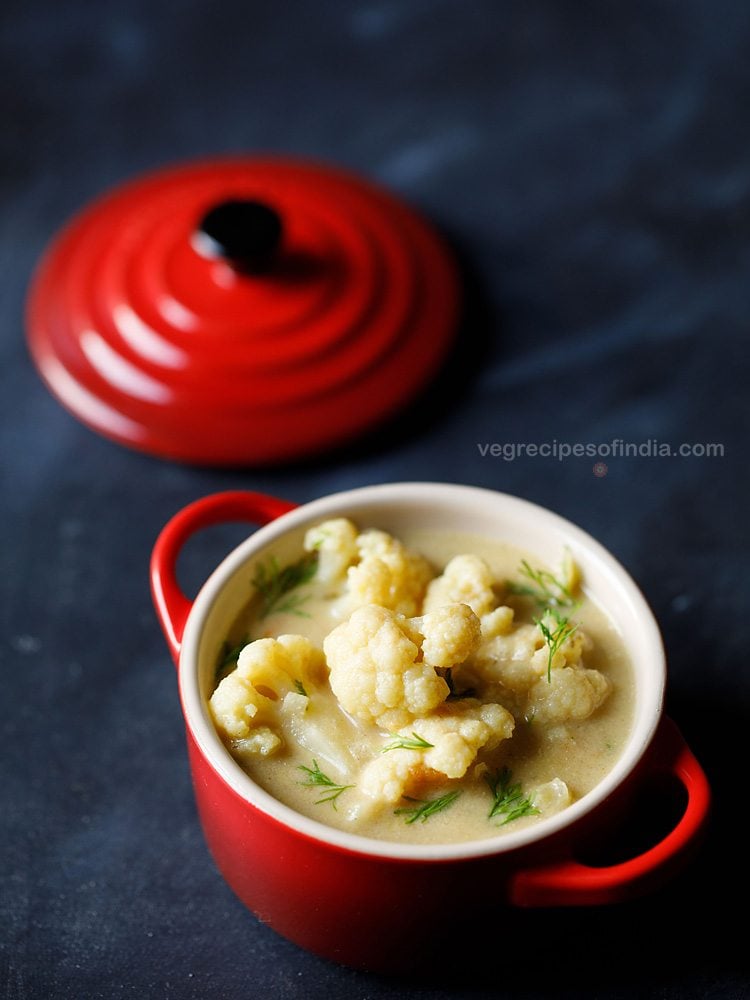 top shot of cauliflower with fresh herbs in liquid broth, served in small red bowl