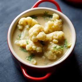 top shot of cauliflower with fresh herbs in kurma gravy, served in small red bowl