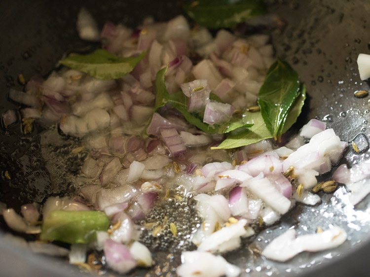 close up shot of onions and curry leaves cooking in saucepan