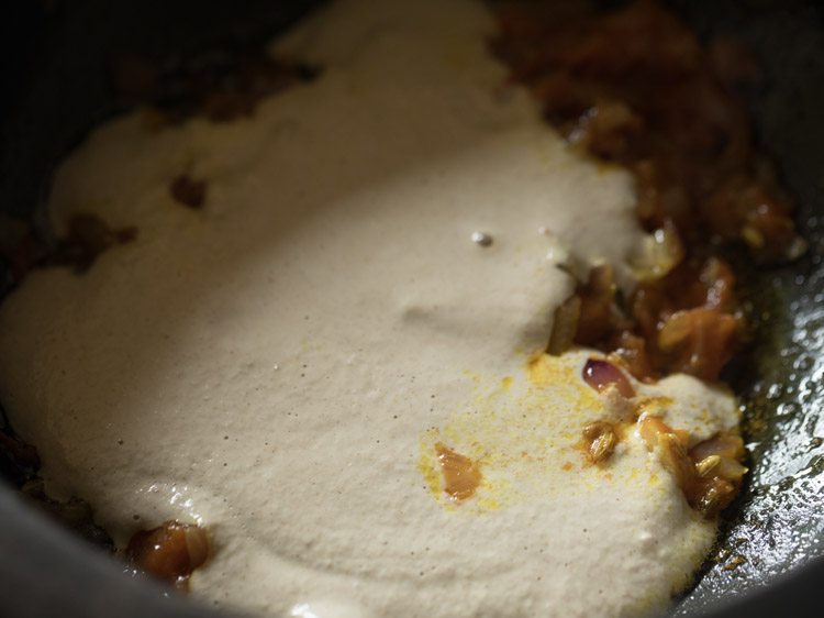 close up shot of cauliflower puree being added to sautéd veggies in saucepan