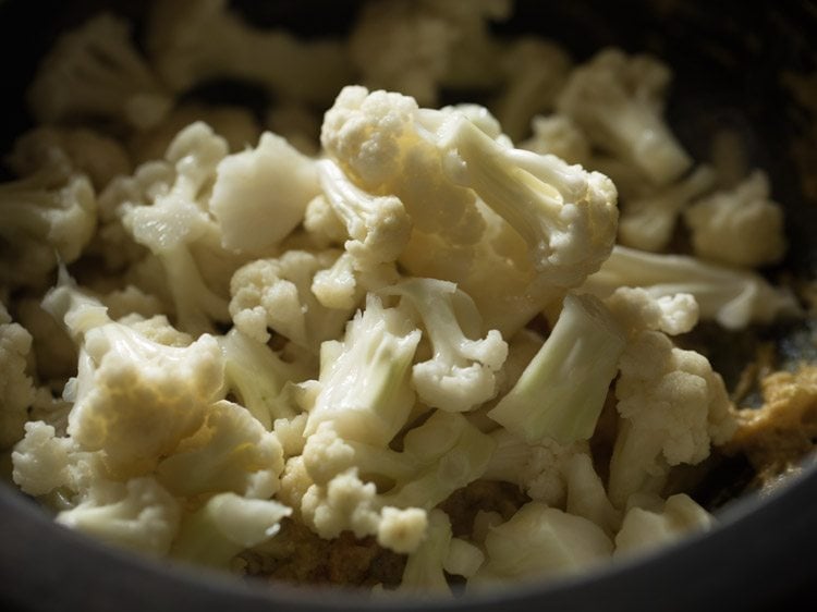 close up of cauliflower being added on top of masala in saucepan