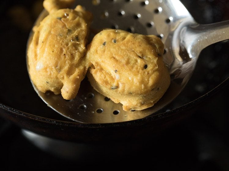 removing fried pakodas with a slotted spoon from hot oil. 