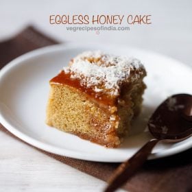 eggless honey cake slice served on a white plate with a spoon kept on right side and text layover.