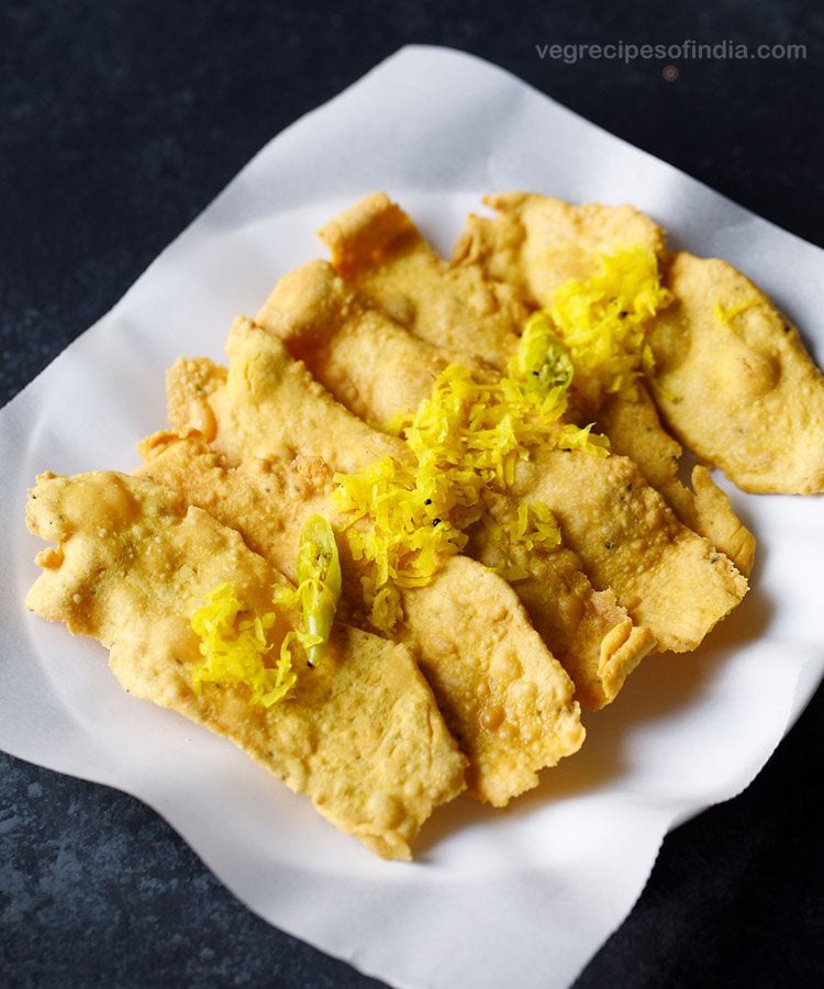 fafda topped with papaya sambharo and served on a butter paper lined plate with text layover. 