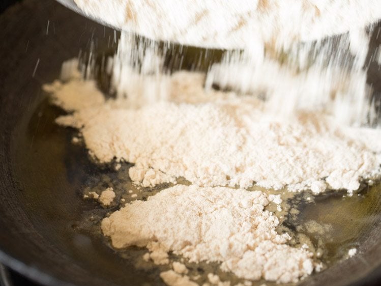 adding whole wheat flour to the melted ghee in pan. 