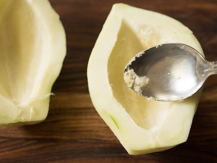 scraping tiny seeds and pith from raw papaya with a spoon. 