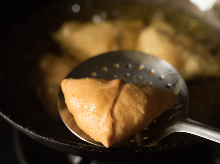 removing fried shingara with a slotted spoon. 