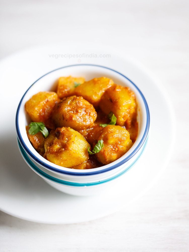 aloo potoler dalna garnished with coriander leaves and served in a blue rimmed white bowl with text layover. 