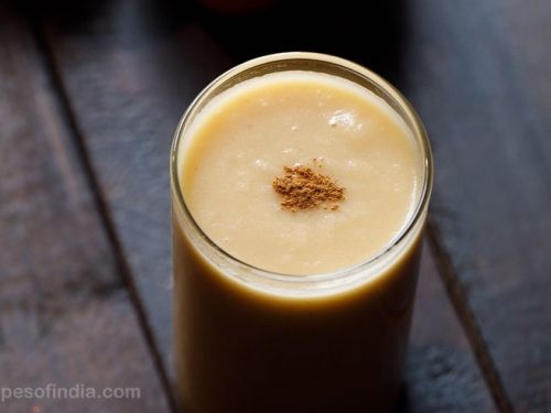 apple smoothie in a glass with a light pinch of ground cinnamon on top of smoothie