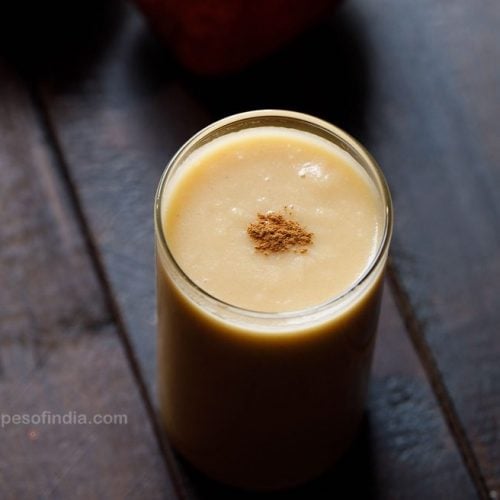 apple smoothie in a glass with a light pinch of ground cinnamon on top of smoothie