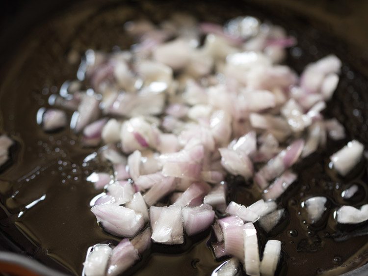 Closeup shot of diced onions being sautéed in oil in saucepan.