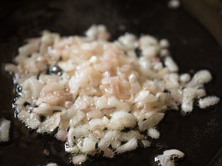 Closeup shot of diced onions sautéing in oil in saucepan.