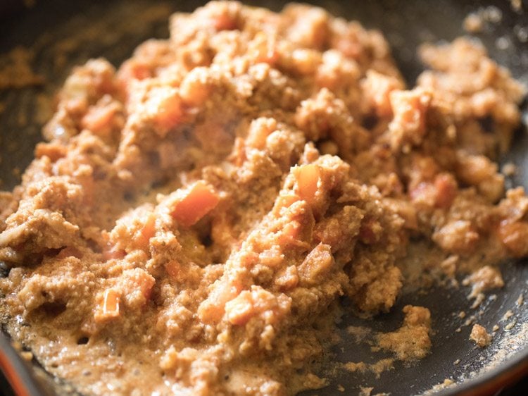 Tomatoes mixed with brinjal curry base cooking in skillet.