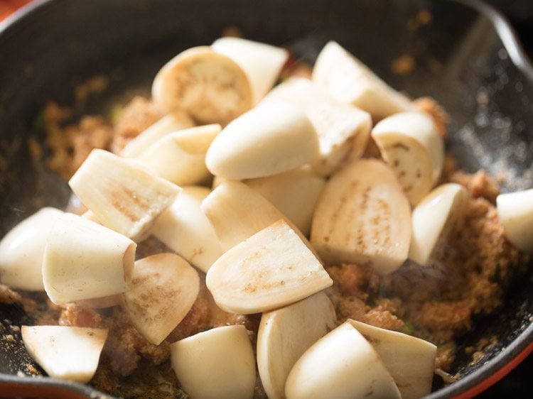 Chopped brinjals added to curry mixture in skillet.