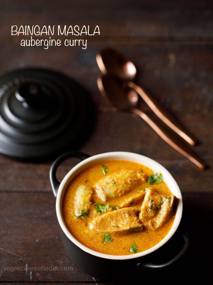 brinjal curry garnished with coriander leaves and served in a black casserole with 2 copper spoons kept in the background and text layover.