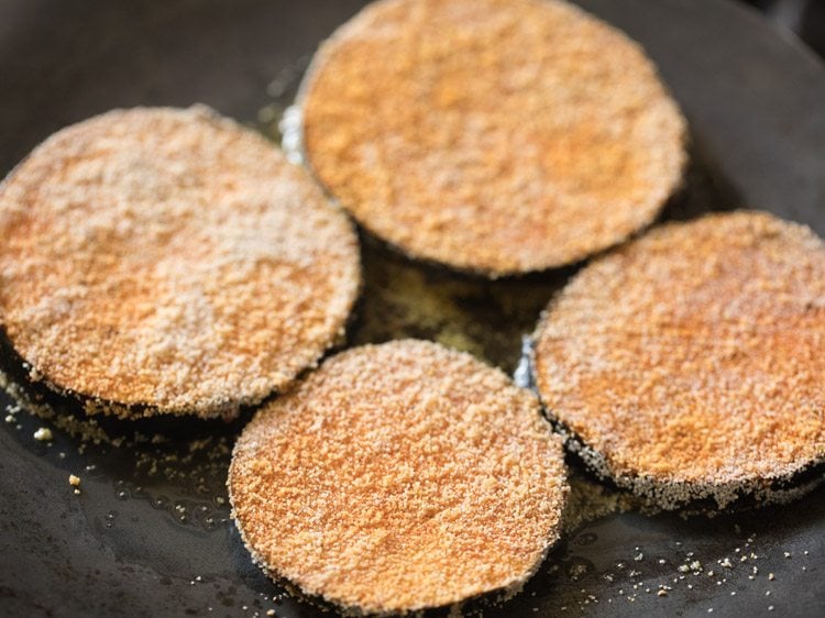 brinjal slices placed in hot oil on pan. 