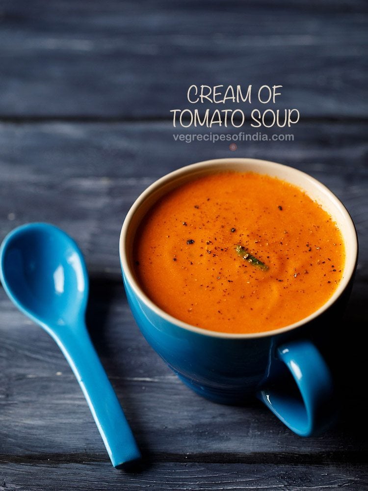 cream of tomato soup served in a large blue mug with a blue spoon kept on the side and text layovers.