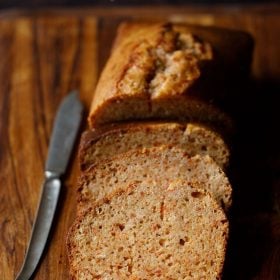 eggless carrot cake loaf sliced halfway on a wooden board with a brass butter knife at side