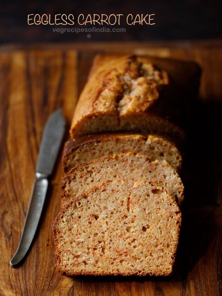 eggless carrot cake loaf sliced halfway on a wooden board with a brass butter knife at side with text layover.