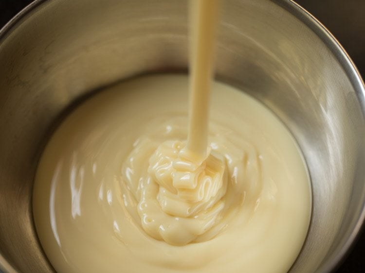 condensed milk being poured in a steel bowl