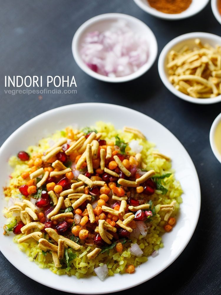 indori poha served on white plate with small bowls of chopped onions and sev kept in the top right side and text layovers.