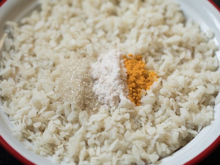 turmeric powder, sugar and salt added to poha in bowl. 