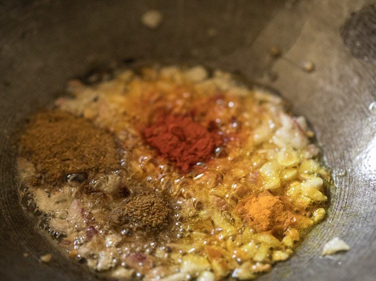 spice powders added to onions in pan. 