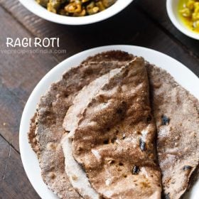 ragi roti smeared with ghee with one roti folded and served on a white plate with a bowl of sabzi and curry kept in the top background and text layover.