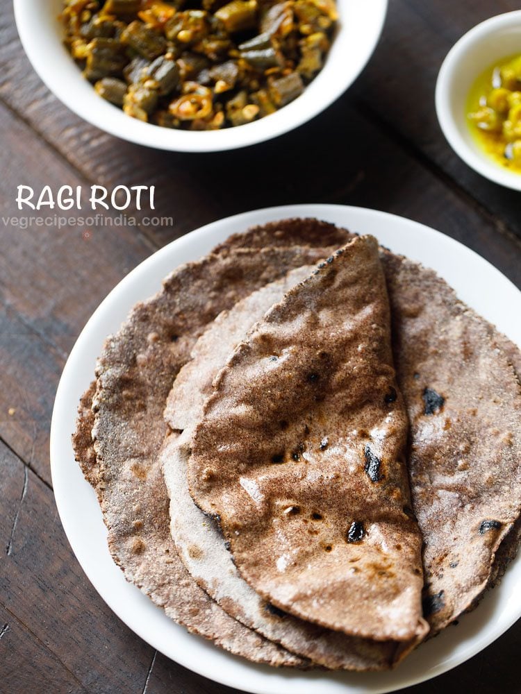 ragi roti smeared with ghee with one roti folded and served on a white plate with a bowl of sabzi and curry kept in the top background and text layover.