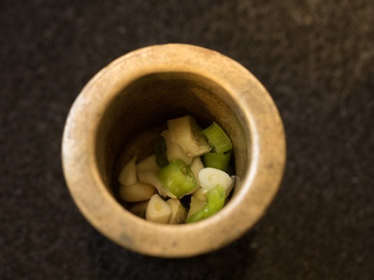 garlic cloves, ginger and chopped green chili added in a mortar for valor papdi nu shaak. 