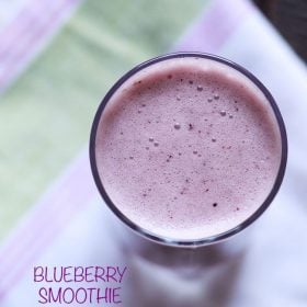 overhead shot of blueberry smoothie in a glass placed on a white, pink and green cotton napkin