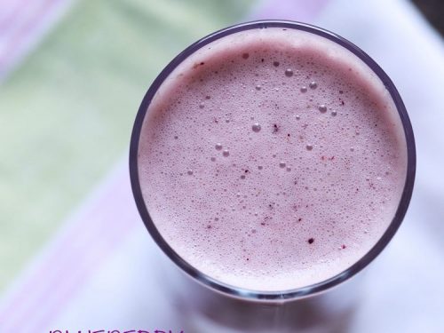 overhead shot of blueberry smoothie in a glass placed on a white, pink and green cotton napkin