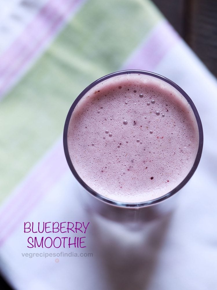 overhead shot of vegan blueberry smoothie in a glass placed on a white, pink and green cotton napkin with text layovers