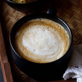 hot coffee served in a black cup kept on a wooden tray.