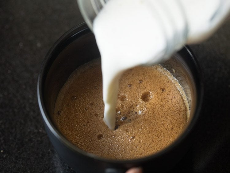 pouring some of the frothed milk into the cup for making cafe style cappuccino with instant coffee.