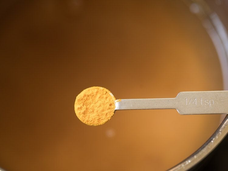 adding turmeric powder to tamarind mixture for coconut milk rasam. 