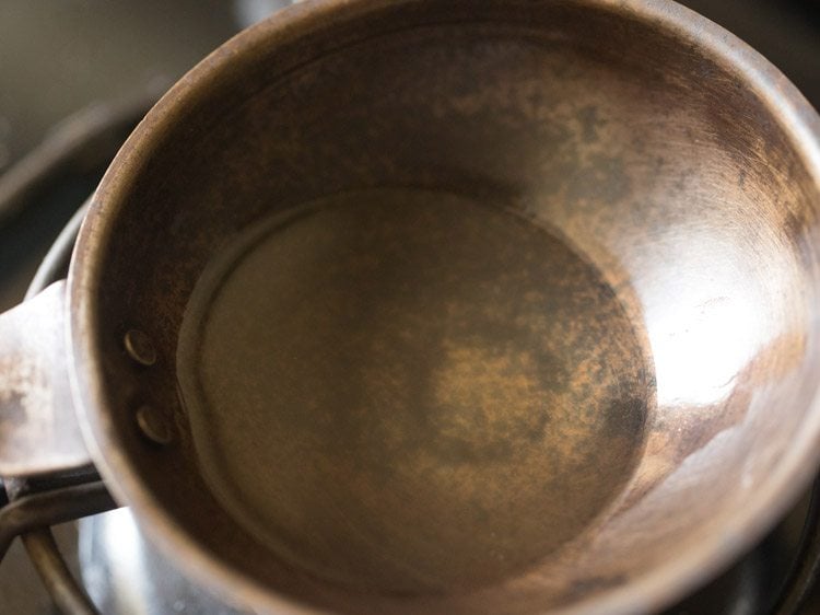 heating coconut oil in a small pan for making tempering for thengai paal rasam.