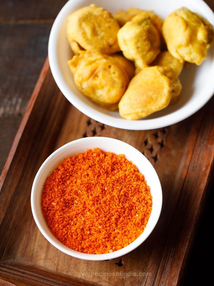 dry garlic coconut chutney (a.k.a. lasun khobra) in a white bowl on a wooden tray next to another white bowl of pakoda snacks.