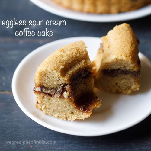 hero shot of two slices of streusel sour cream coffee cake on a white plate with the rest of the cake in the background.