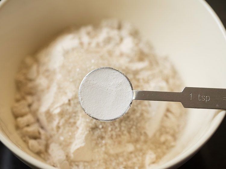 Baking powder in teaspoon measurer held above mixing bowl of whole wheat flour.