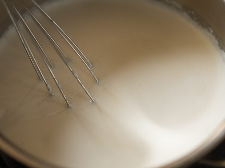 Whisk mixing milk in saucepan for eggless waffle recipe.