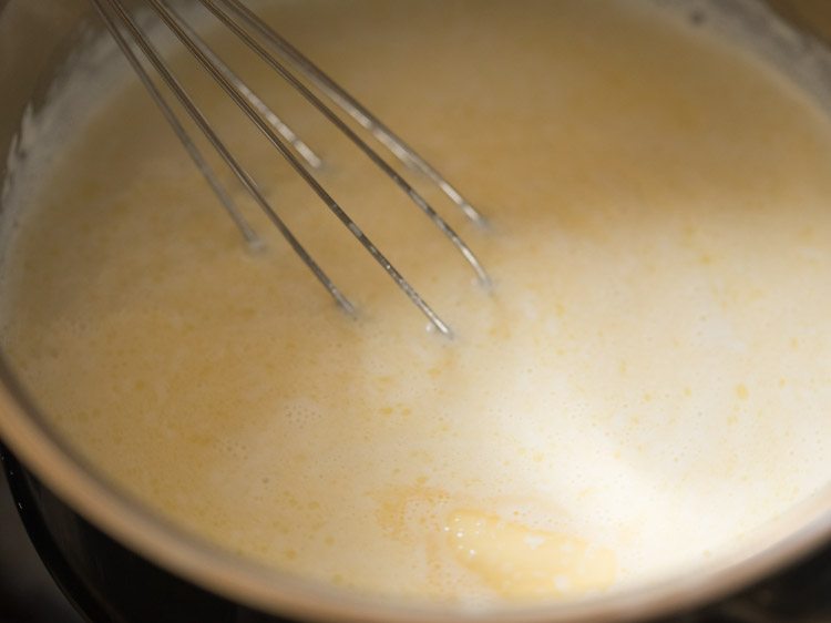 Whisk mixing milk and butter in saucepan for eggless waffle recipe.