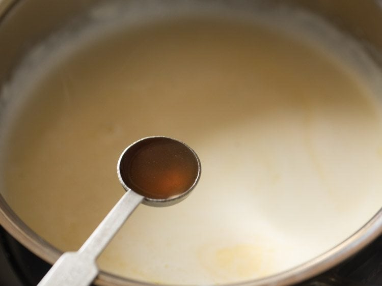 Vanilla in teaspoon measurer held over saucepan with milk.