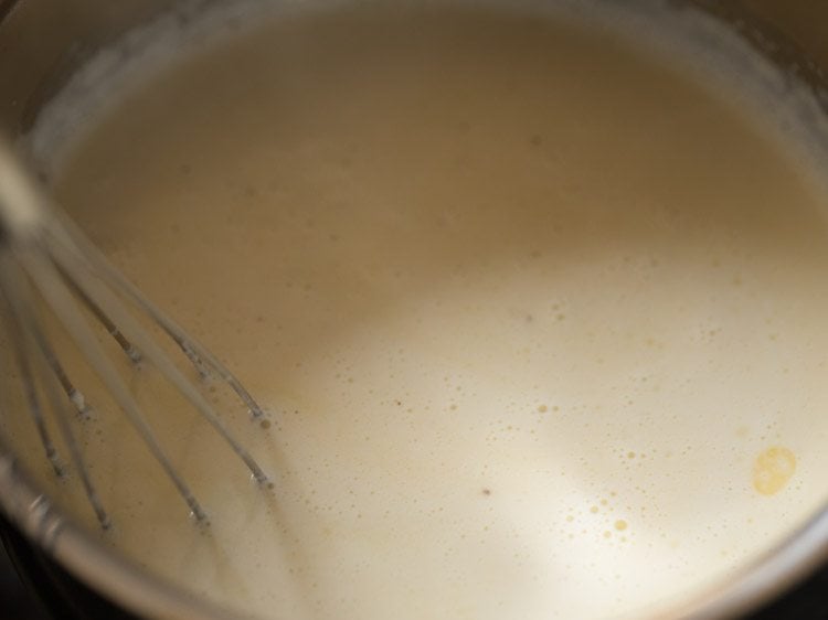 Whisk mixing milk and butter in saucepan for eggless waffle recipe.